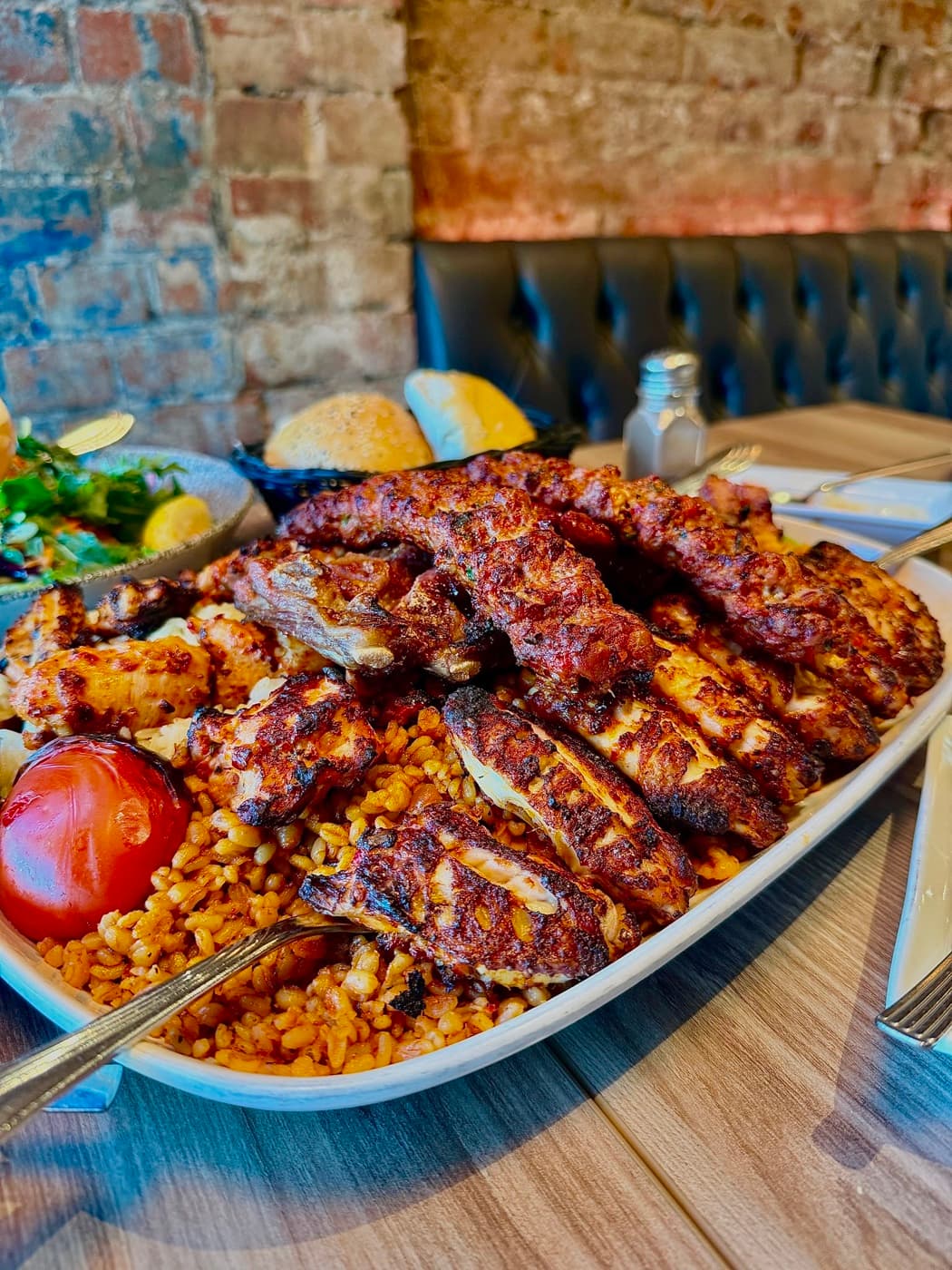 The family platter at Antep Kitchen Oxford: chicken shish, lamb ribs and adana köfte over bulgur rice with a grilled tomato, against an exposed brick wall