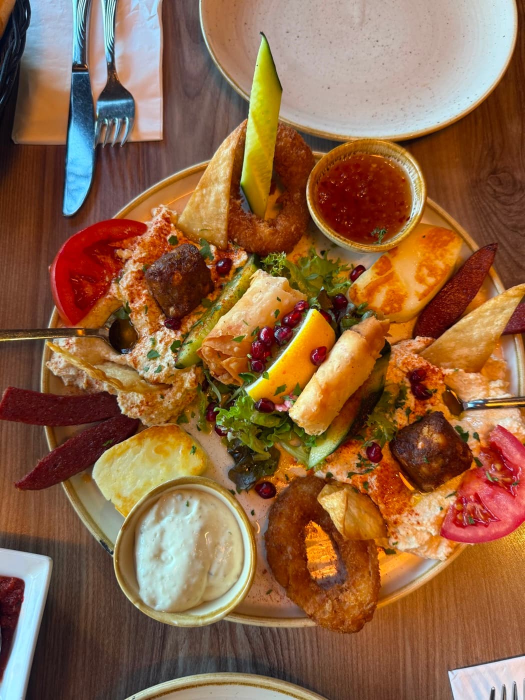 The mixed hot mezze board at Antep Kitchen Oxford seen from above: halloumi, sigara böreği, calamari rings, falafel, sucuk, tomato and pomegranate seeds around a bowl of dip