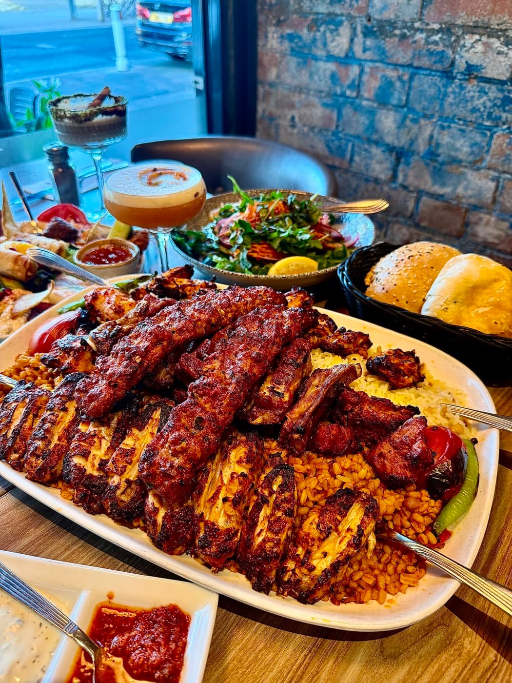 The family platter at Antep Kitchen Oxford: lamb ribs, chicken shish, adana köfte and lamb shish piled over bulgur rice, with a side salad, bread basket and an espresso martini on the table