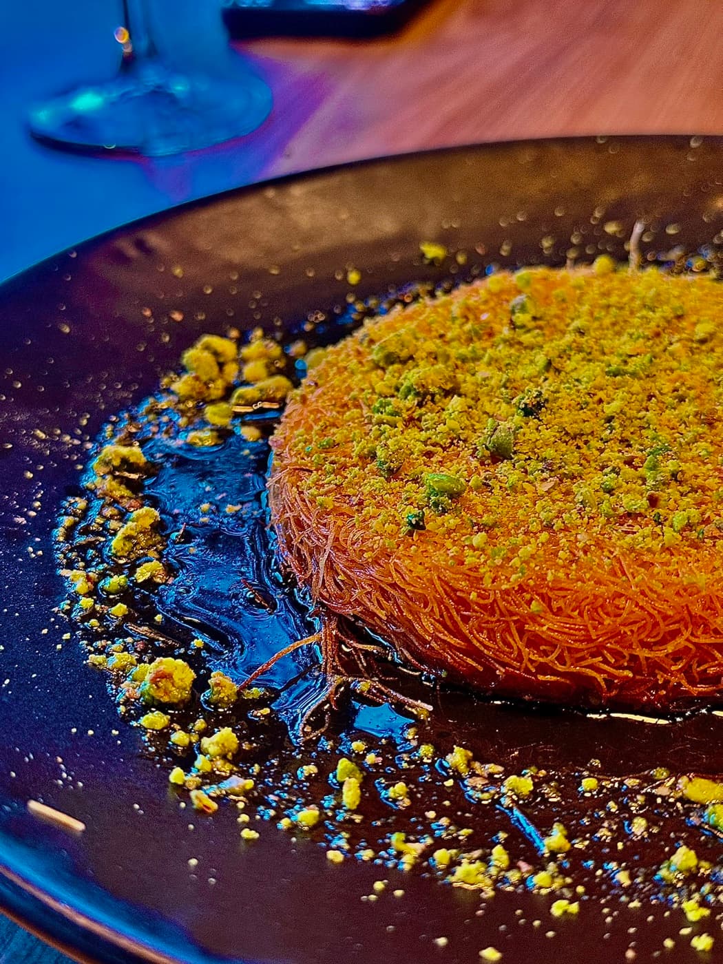 Künefe at Antep Kitchen Oxford: a round of shredded pastry in syrup topped with crushed pistachio on a black plate