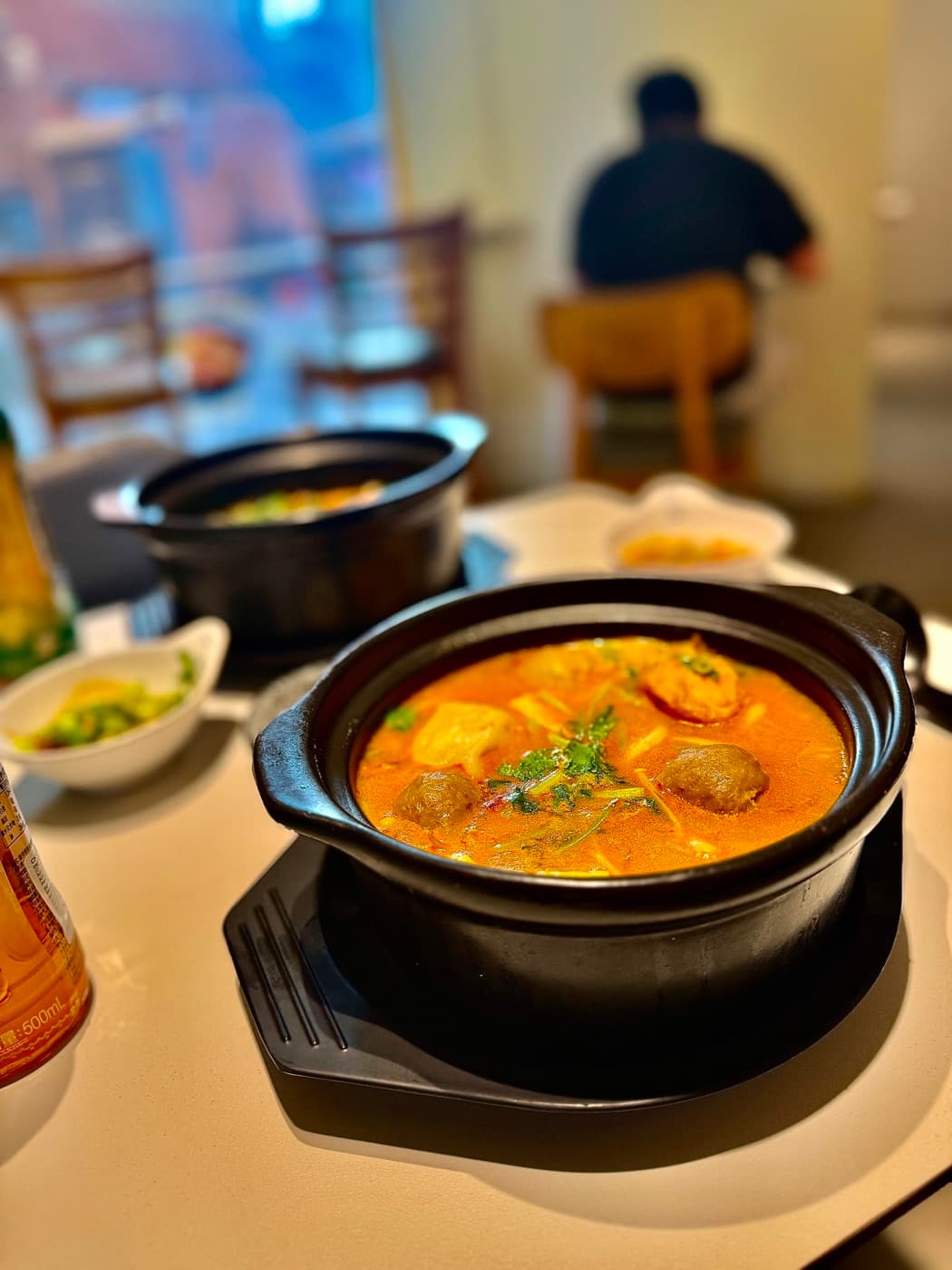 The spicy and sour golden broth hot pot at Mr. Wang Hot Pot Oxford, an individual clay pot of golden broth with a dumpling, meatballs, tofu skin and fresh coriander
