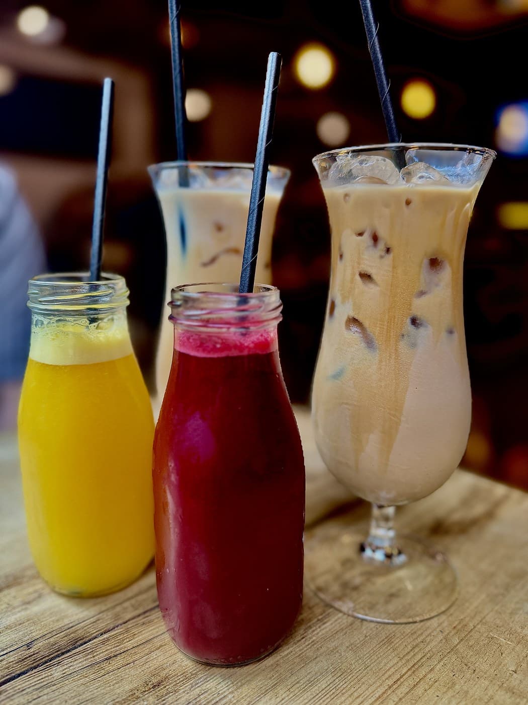 Drinks at Oxford Brunch Bar lined up on the table: a bottle of fresh orange juice, a bottle of deep red Super Juice and two iced Jericho Coffee Traders lattes