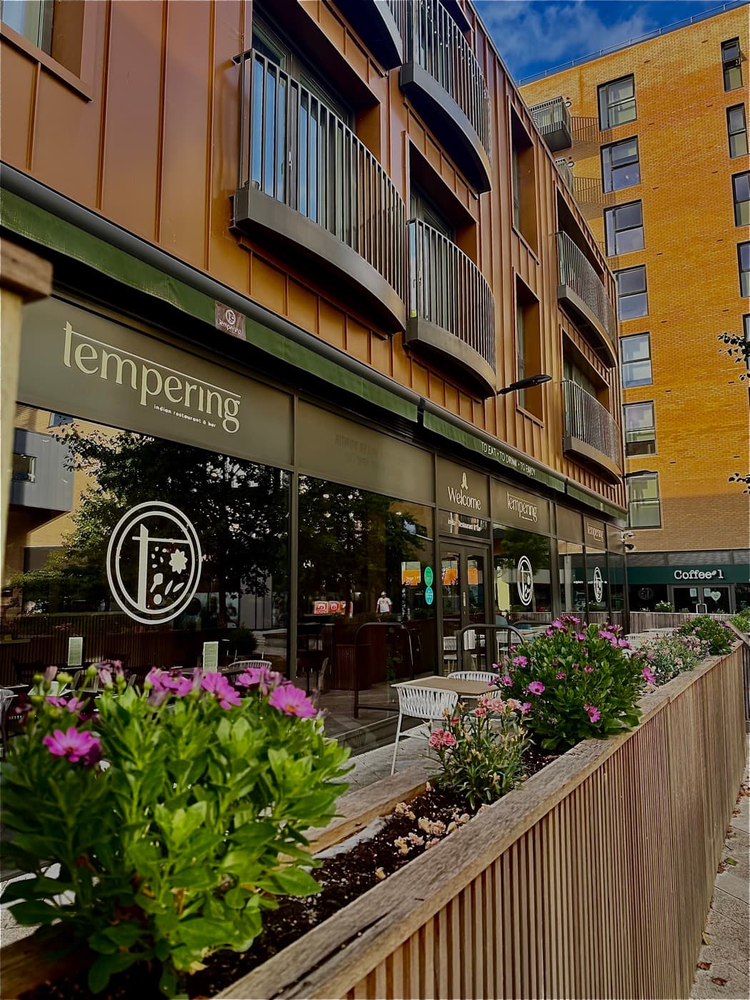 Tempering's exterior on West Way Square in Botley, Oxford, with green signage and outdoor seating framed by flower planters