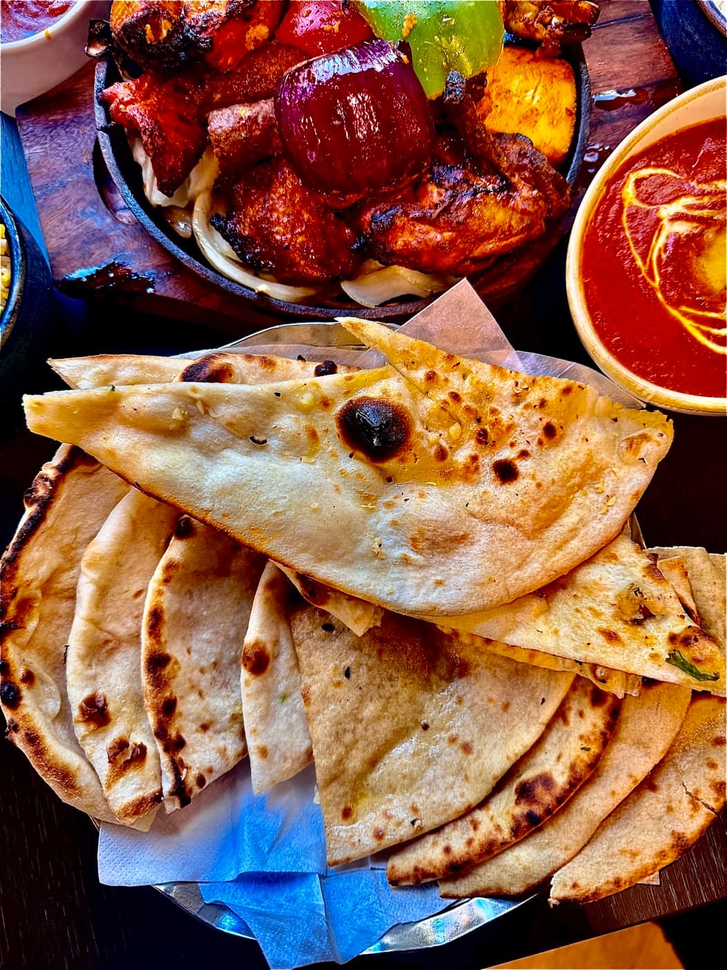 A basket of freshly made breads at Tempering — tandoori roti, garlic naan and peshwari naan — beside a tandoori grill and curry